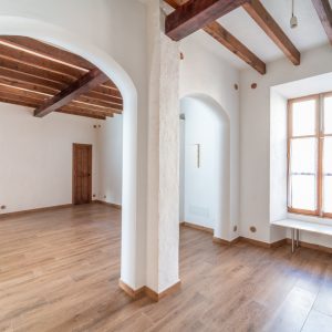 Detail of a living room area with arches, a window, wooden floors and beams.